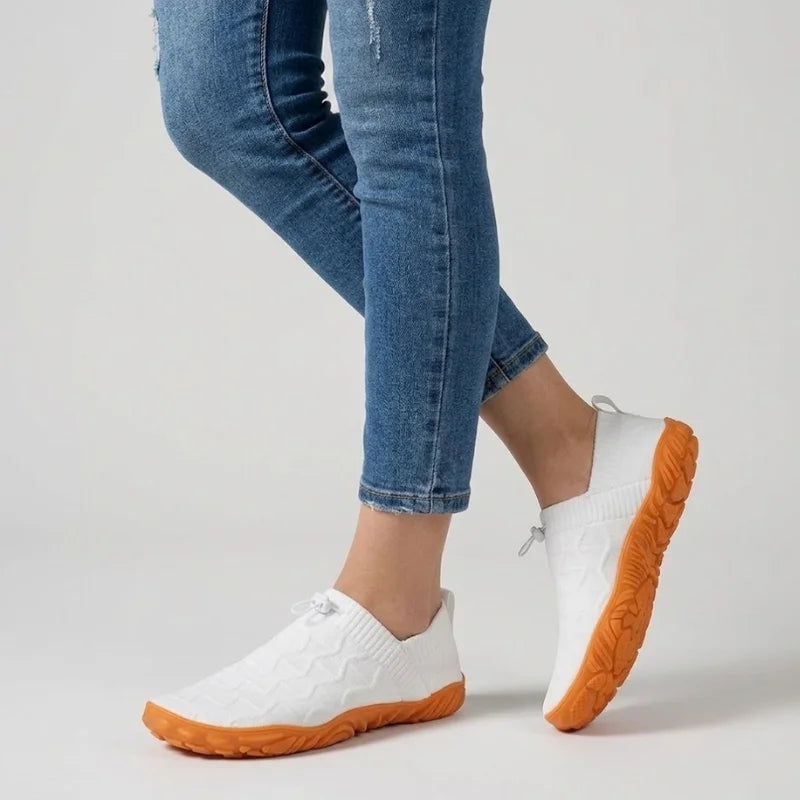 Person in Jeans geht in weißen Glidevo Slippern
